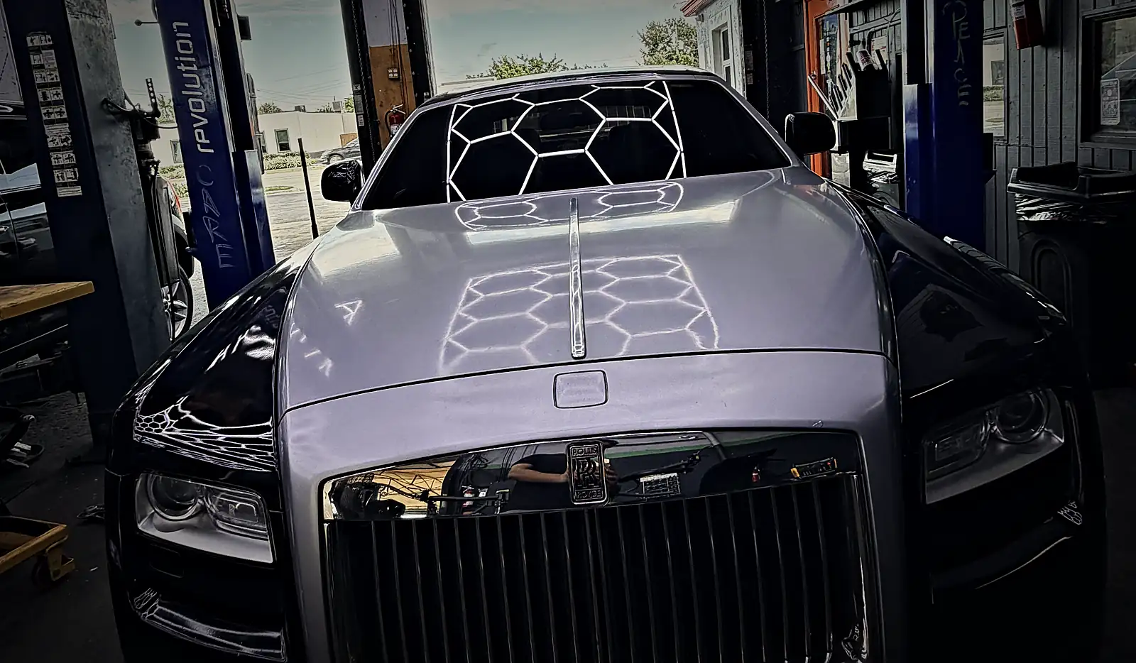 Modern Rolls-Royce Ghost in a Prestige service bay under the hexagon-light ceiling